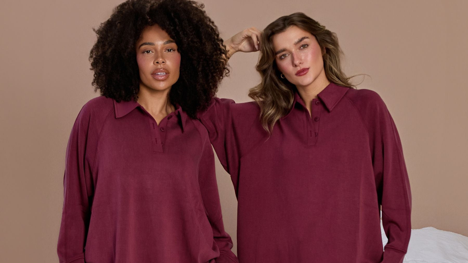 Two women wearing matching burgundy loungewear sets on a beige background.