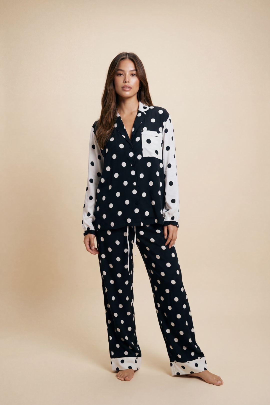 Woman wearing a black and white polka dot pajama set on a beige background