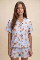 Woman wearing a pajama set with orange and bottle pattern on a beige background