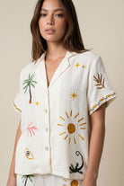 Woman wearing a white shirt with colorful embroidered designs on a beige background