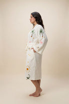 Woman wearing a white robe with palm tree and sun designs on a beige background