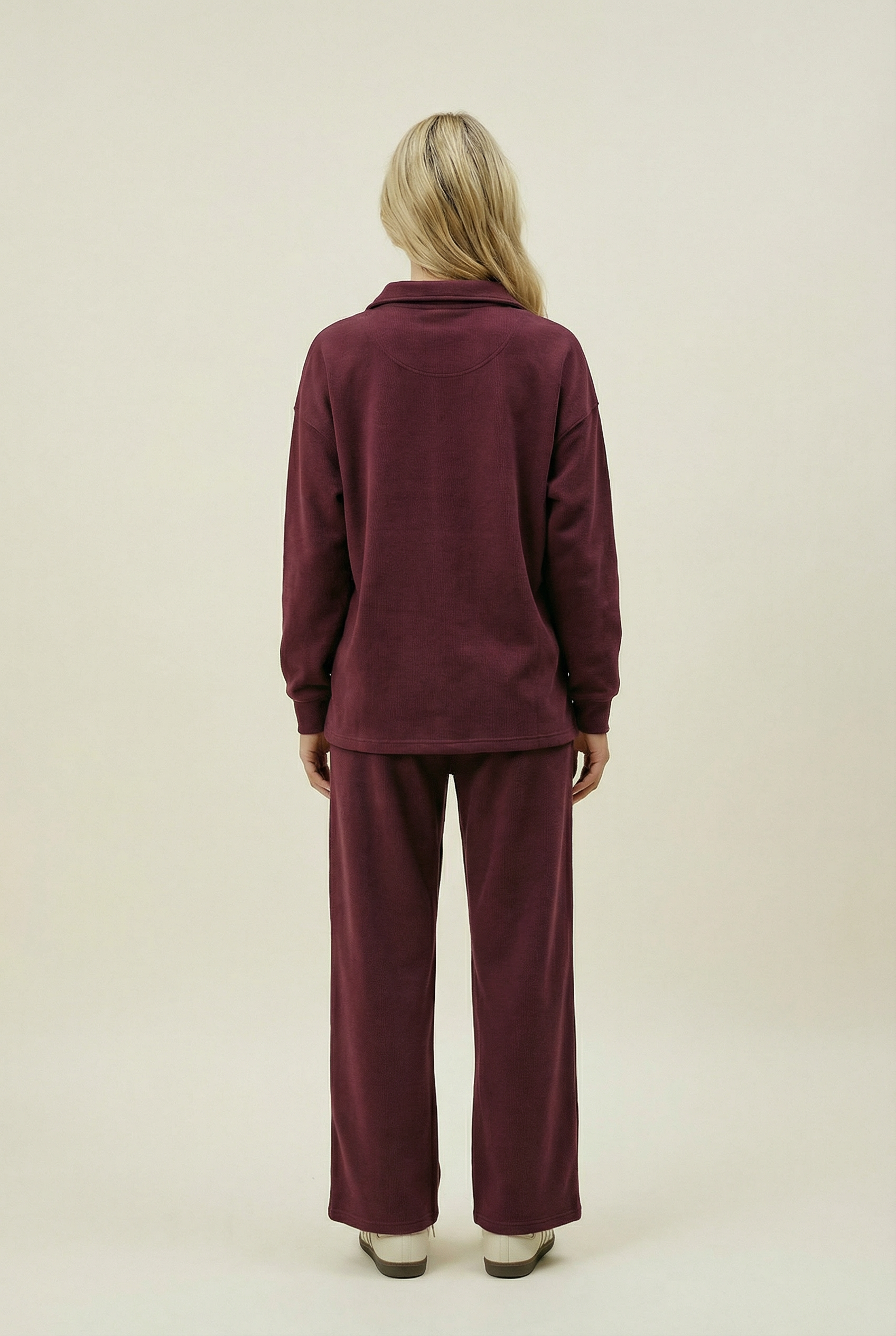 Person wearing a burgundy tracksuit on a beige background