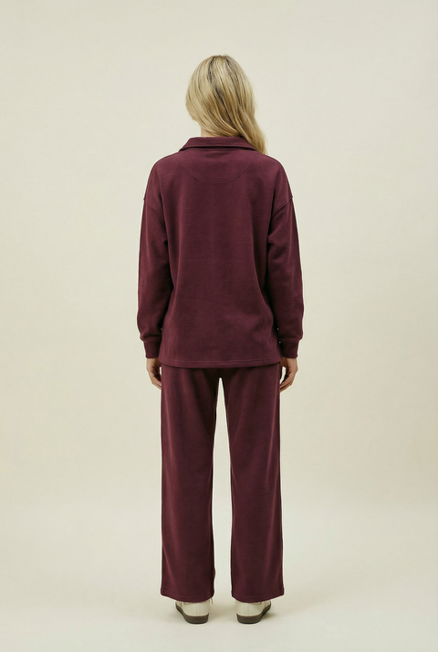 Person wearing a burgundy tracksuit on a beige background