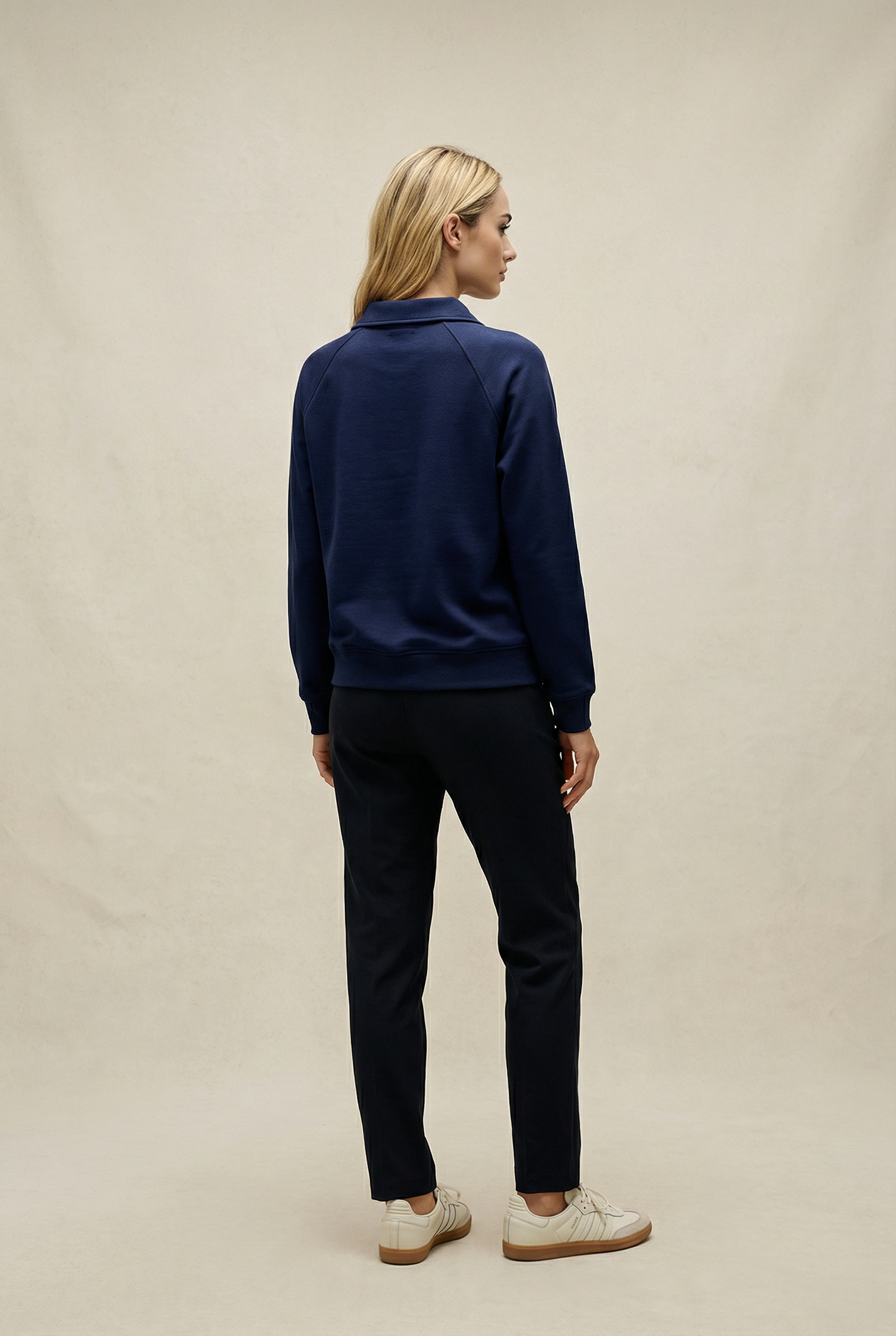 Person wearing a navy blue jacket and black pants on a beige background