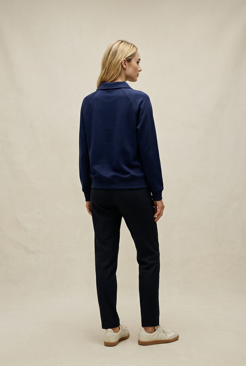 Person wearing a navy blue jacket and black pants on a beige background